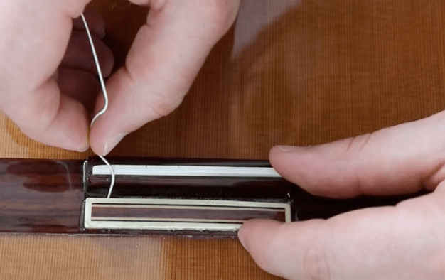 passage d'une corde de guitare dans le chevalet