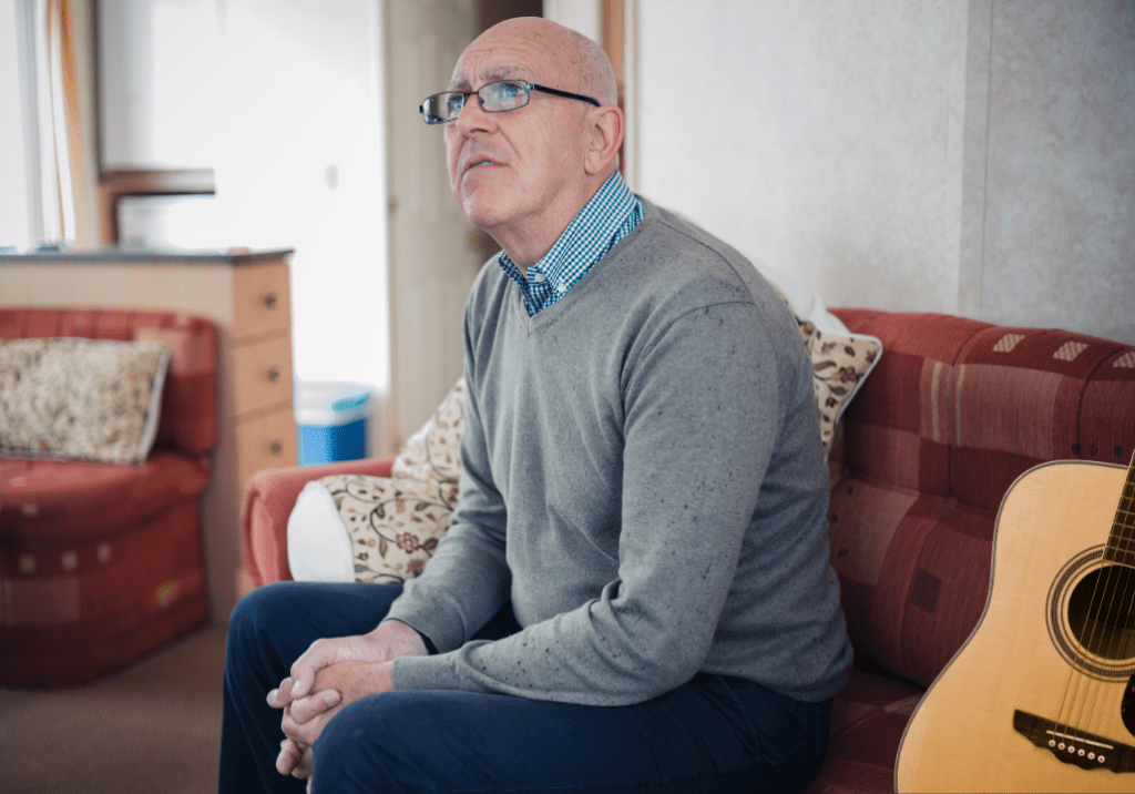 Homme retraité assis sur un canapé avec une guitare à côté de lui